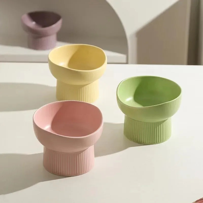 Three colorful ceramic cups (yellow, pink, green) on a light surface.