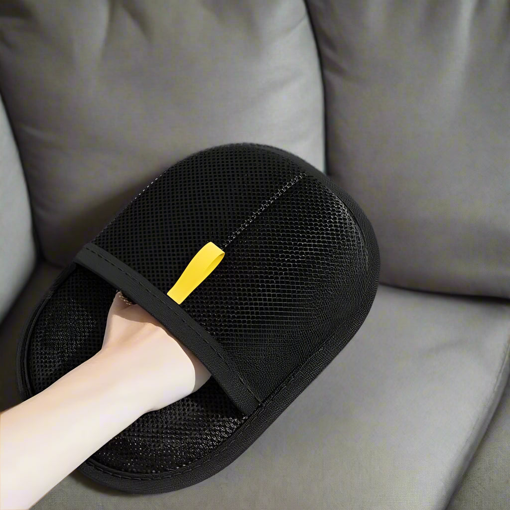 Black electrostatic hair removal gloves with a hand wearing them, on a gray surface with cat hair.