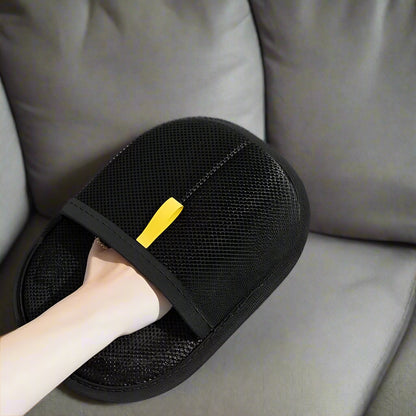 Black electrostatic hair removal gloves with a hand wearing them, on a gray surface with cat hair.